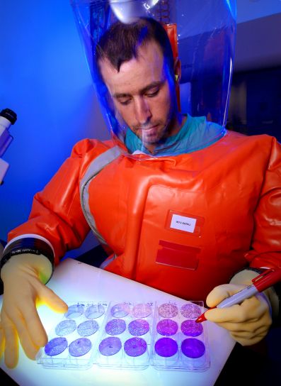 A scientist in a biocontainment suit counting viral plaques.