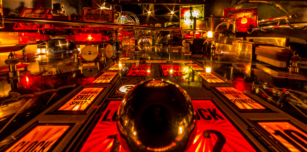 ”A close up image of a ball inside brightly lit pinball machine.